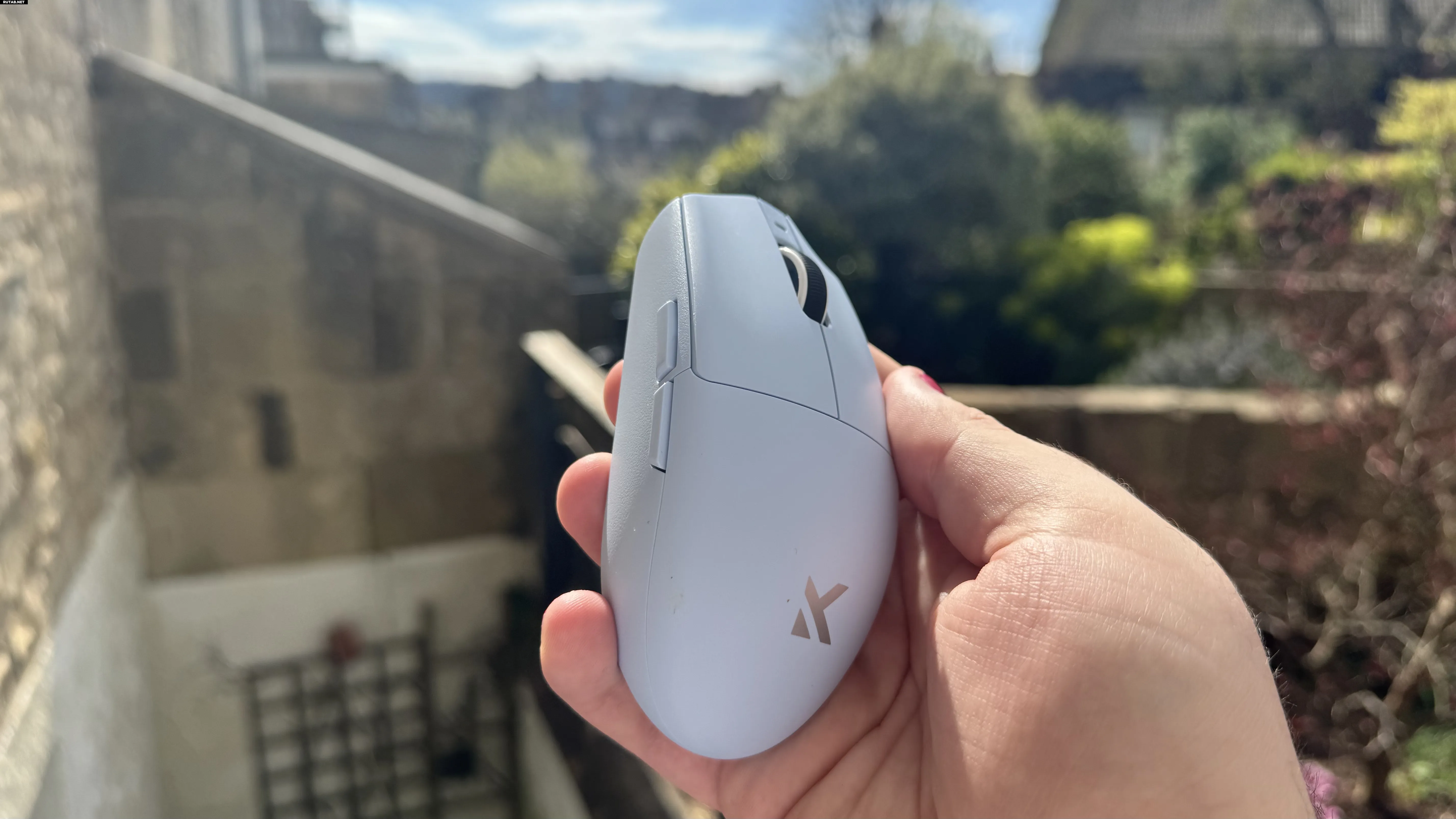 Синяя игровая мышь Mchose G3 V2 сбоку, в руке на фоне сада