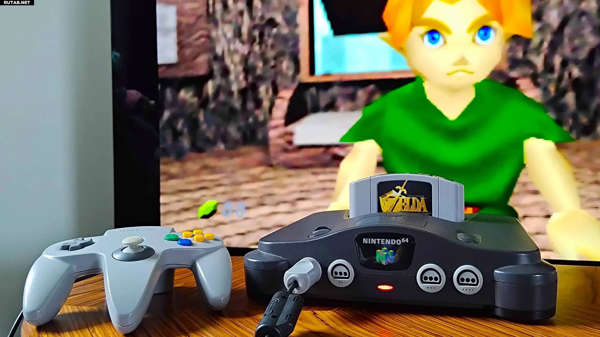 Крупный план модифицированной N64 с HDMI на журнальном столике, на фоне телевизора игра The Legend of Zelda: Ocarina of Time